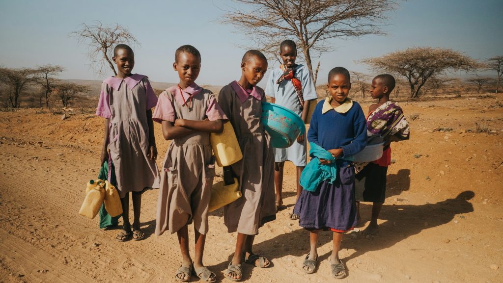 African girls in school uniform holding water bottles and bowls.